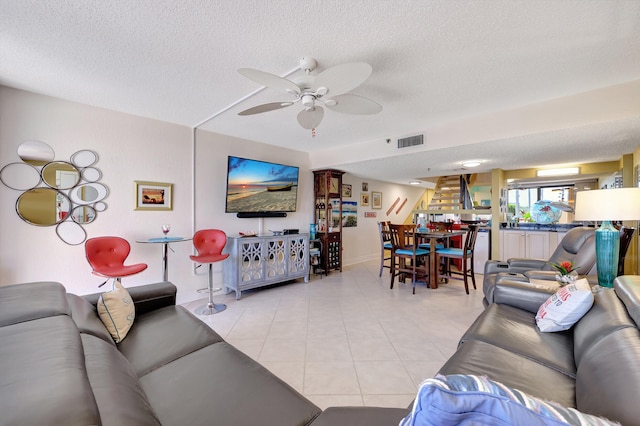 living room with a textured ceiling, ceiling fan, and light tile patterned floors