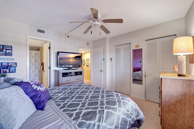 bedroom with ceiling fan, multiple closets, light carpet, and a textured ceiling