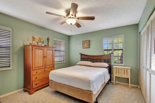 bedroom featuring a textured ceiling, ceiling fan, light carpet, and a closet