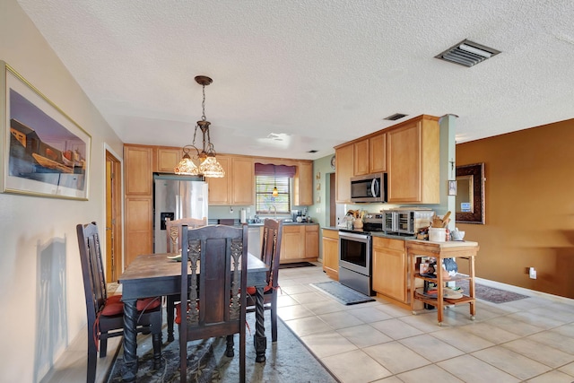 kitchen featuring stainless steel appliances, a textured ceiling, decorative light fixtures, light brown cabinetry, and light tile patterned floors