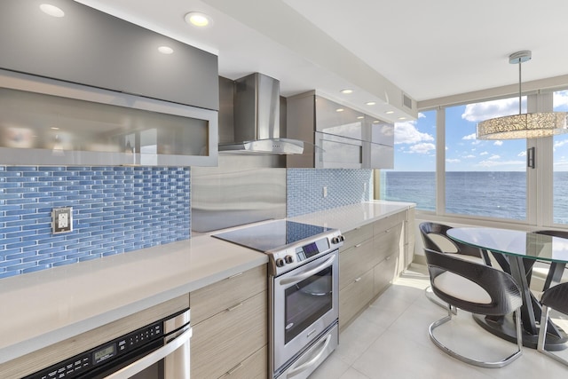 kitchen featuring wall chimney exhaust hood, a water view, tasteful backsplash, pendant lighting, and stainless steel appliances