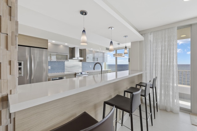 kitchen with pendant lighting, kitchen peninsula, wall chimney exhaust hood, and appliances with stainless steel finishes