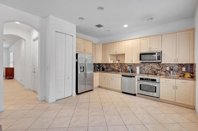 kitchen featuring light stone counters, backsplash, cream cabinetry, light tile patterned floors, and appliances with stainless steel finishes