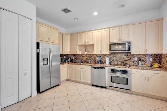 kitchen with stainless steel appliances, light stone counters, backsplash, cream cabinetry, and light tile patterned floors