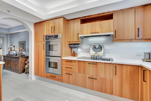 kitchen featuring black electric stovetop, stainless steel double oven, light brown cabinetry, and tasteful backsplash