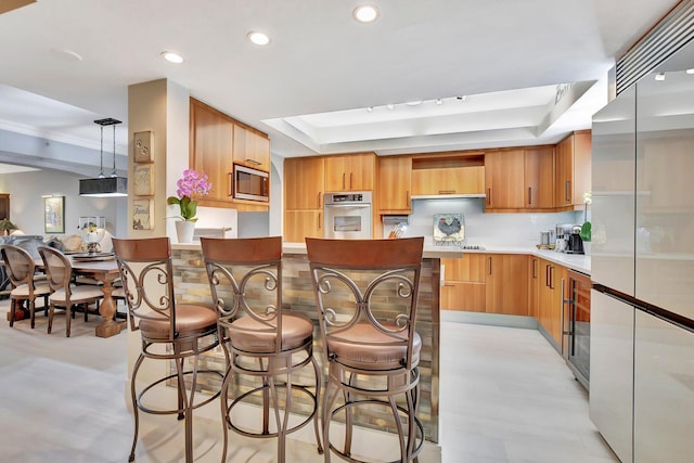 kitchen with built in appliances, decorative light fixtures, and a tray ceiling