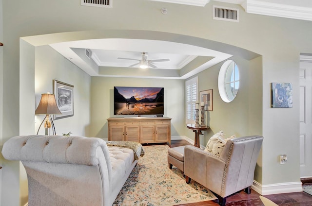 living room with ceiling fan, a tray ceiling, and ornamental molding