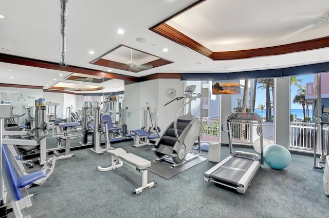 gym featuring carpet flooring, ceiling fan, and a tray ceiling