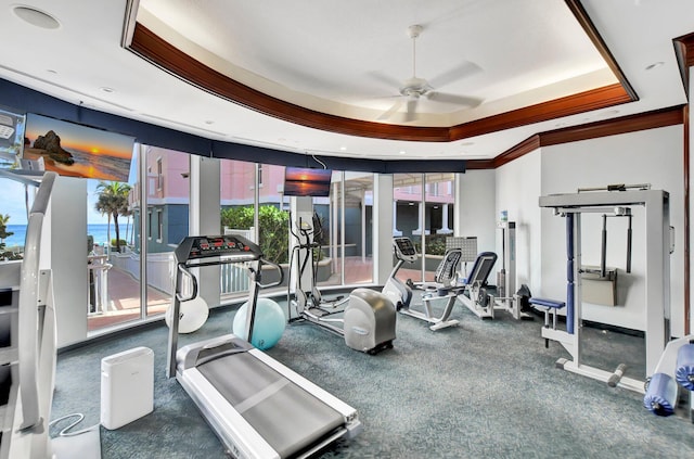 gym with a raised ceiling, ceiling fan, and crown molding