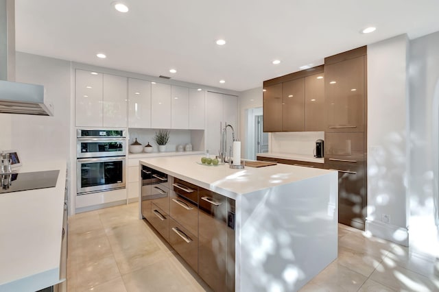 kitchen featuring stainless steel double oven, white cabinets, black electric cooktop, a kitchen island with sink, and light tile patterned flooring