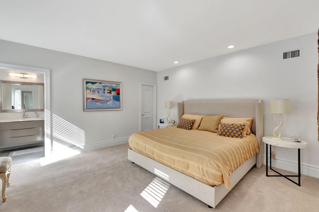 bedroom with ensuite bath, light carpet, and sink