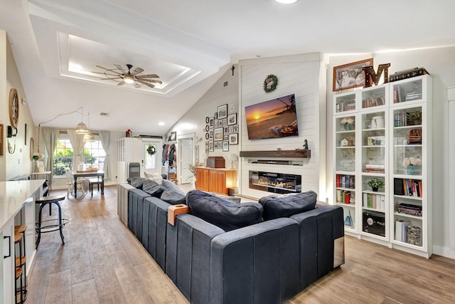 living room featuring ceiling fan, a fireplace, light hardwood / wood-style floors, and lofted ceiling