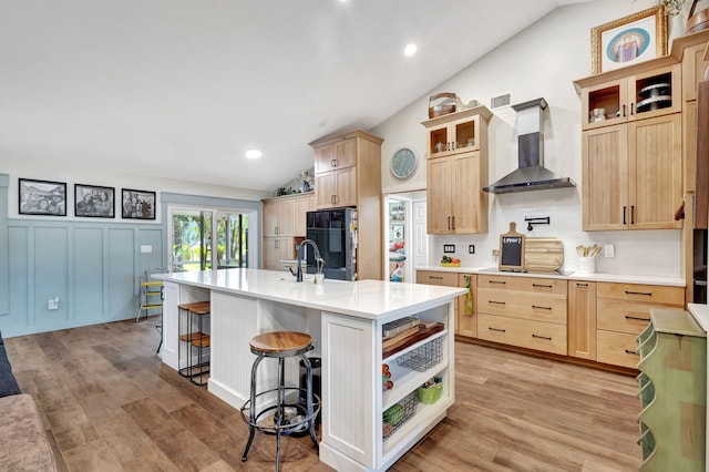 kitchen featuring light brown cabinets, wall chimney exhaust hood, an island with sink, and lofted ceiling