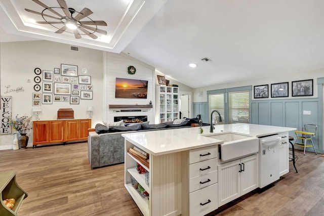 kitchen with a large fireplace, dishwasher, sink, an island with sink, and white cabinets