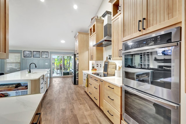 kitchen with wall chimney exhaust hood, light brown cabinetry, sink, and appliances with stainless steel finishes