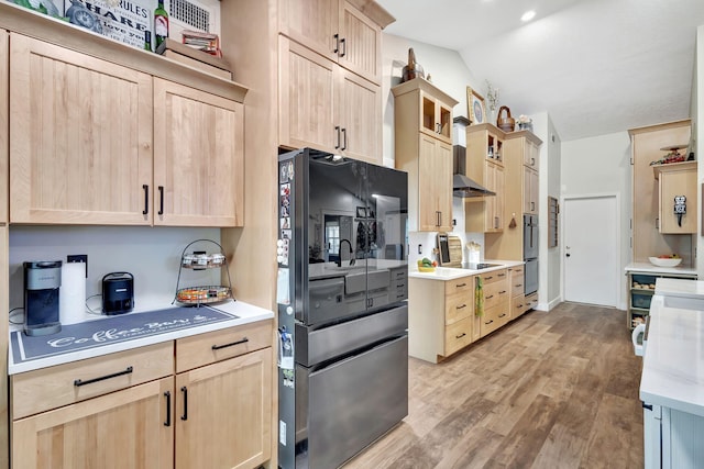 kitchen with black refrigerator, cooktop, light brown cabinetry, and vaulted ceiling