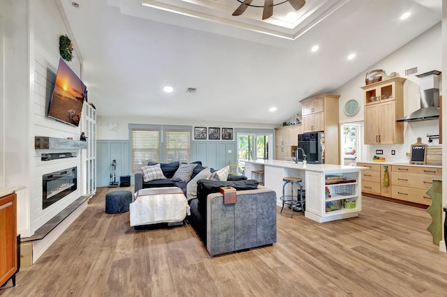 living room featuring a fireplace, light wood-type flooring, vaulted ceiling, and ceiling fan