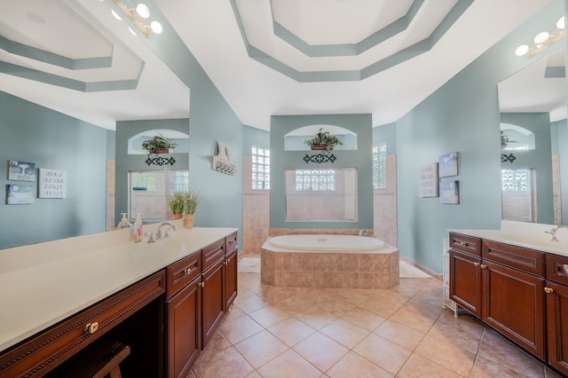 bathroom featuring a garden tub, a tray ceiling, two vanities, and a sink