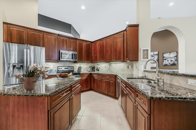 kitchen with light tile patterned floors, backsplash, appliances with stainless steel finishes, a sink, and dark stone counters