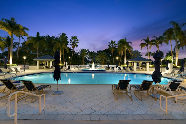 pool at dusk featuring a gazebo and a patio