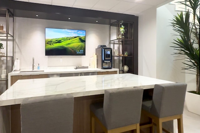 bar with a paneled ceiling, light stone countertops, and sink