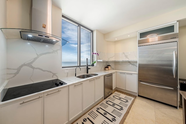 kitchen with wall chimney range hood, sink, appliances with stainless steel finishes, light stone counters, and white cabinets