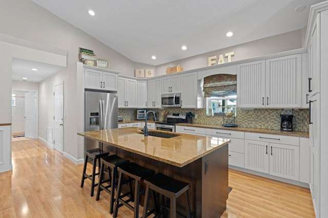 kitchen with lofted ceiling, a kitchen island with sink, sink, appliances with stainless steel finishes, and a kitchen bar