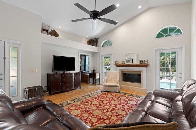 living room featuring ceiling fan, a fireplace, high vaulted ceiling, and light hardwood / wood-style flooring