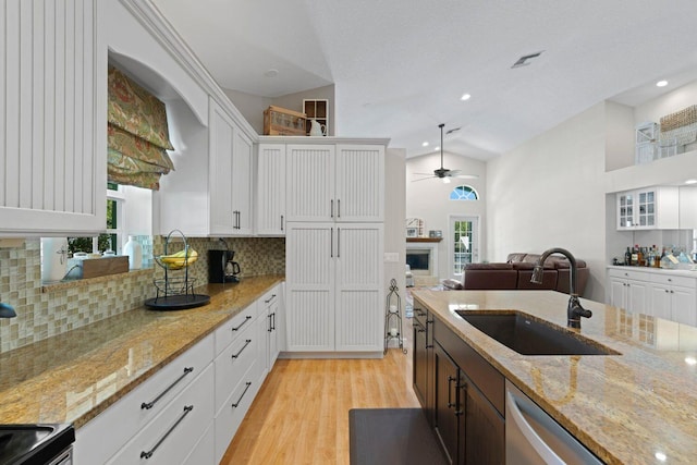 kitchen featuring light wood-type flooring, light stone counters, vaulted ceiling, sink, and white cabinetry