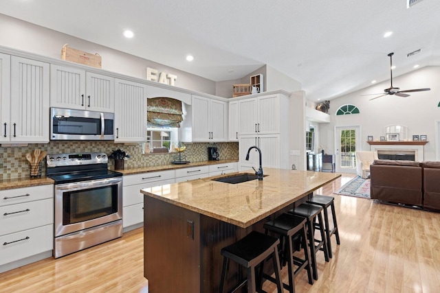 kitchen featuring appliances with stainless steel finishes, vaulted ceiling, sink, a center island with sink, and white cabinets