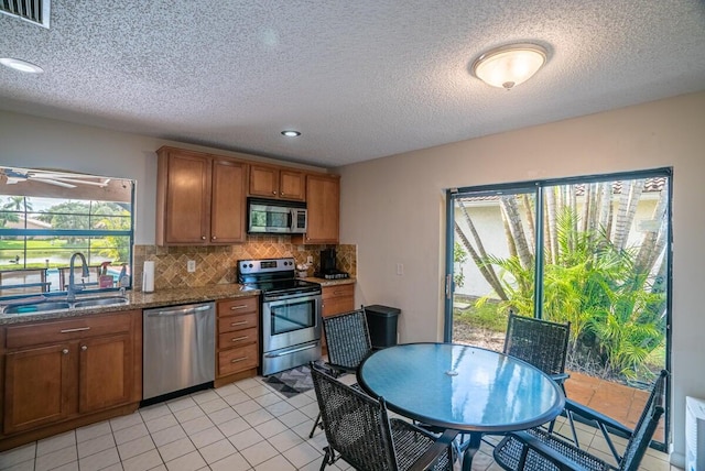 kitchen featuring sink, decorative backsplash, a textured ceiling, appliances with stainless steel finishes, and stone countertops