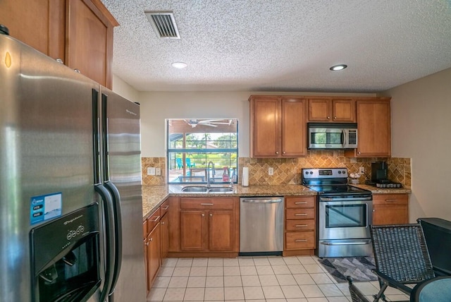 kitchen with light stone countertops, sink, stainless steel appliances, backsplash, and light tile patterned floors