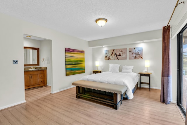 bedroom with a sink, light wood-style floors, baseboards, and a textured ceiling