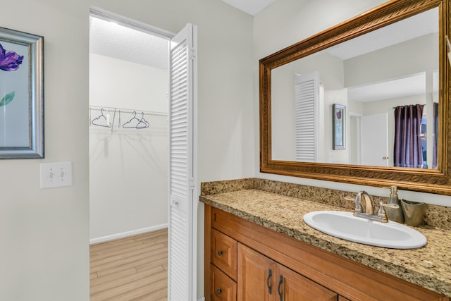 bathroom featuring baseboards, wood finished floors, a walk in closet, a textured ceiling, and vanity