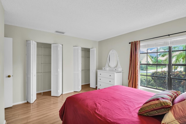 bedroom featuring a textured ceiling, light wood-style flooring, visible vents, baseboards, and two closets