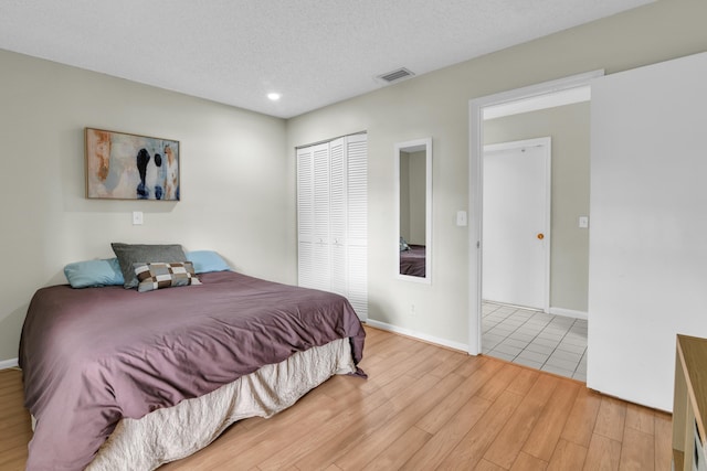 bedroom featuring baseboards, visible vents, light wood-style flooring, a textured ceiling, and a closet