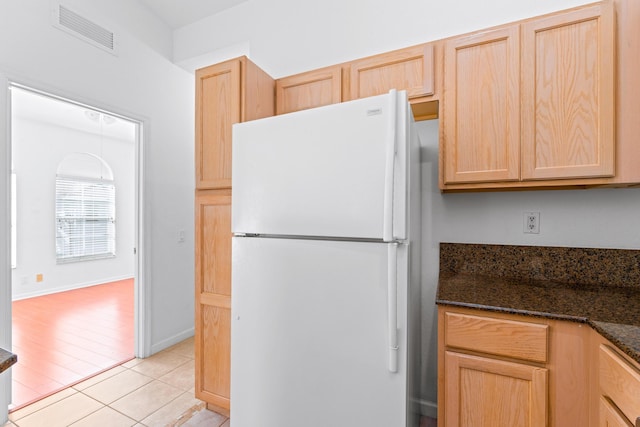 kitchen featuring light brown cabinetry, light tile patterned floors, dark stone counters, and white refrigerator