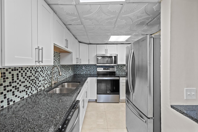 kitchen with white cabinetry, stainless steel appliances, dark stone countertops, sink, and light tile patterned floors