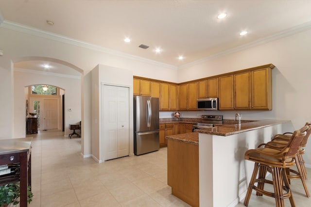 kitchen featuring stainless steel appliances, kitchen peninsula, dark stone counters, light tile patterned flooring, and ornamental molding