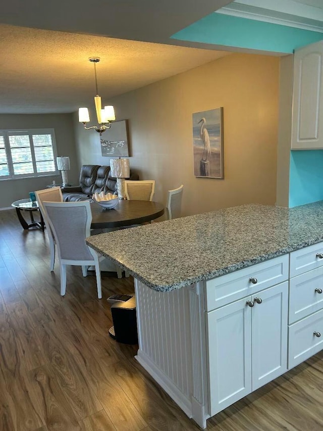 kitchen featuring white cabinets, dark hardwood / wood-style flooring, light stone counters, and hanging light fixtures