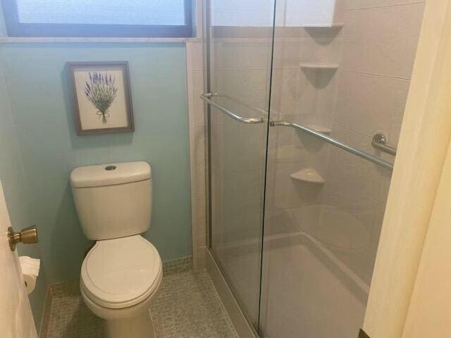 bathroom featuring tile patterned floors, toilet, and a shower with door