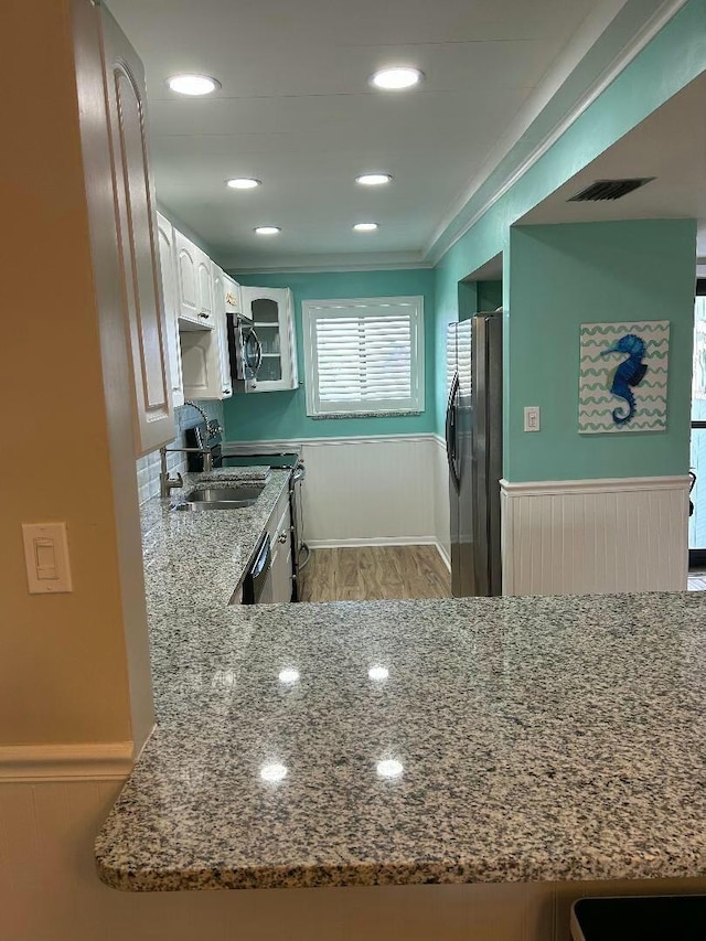 kitchen with light wood-type flooring, ornamental molding, appliances with stainless steel finishes, stone countertops, and white cabinetry