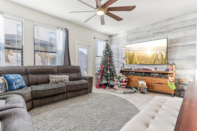 living room featuring ceiling fan, wooden walls, and light tile patterned flooring