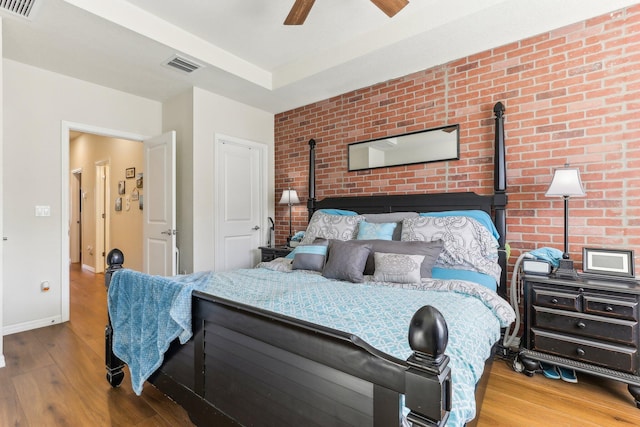 bedroom featuring hardwood / wood-style flooring, ceiling fan, and brick wall