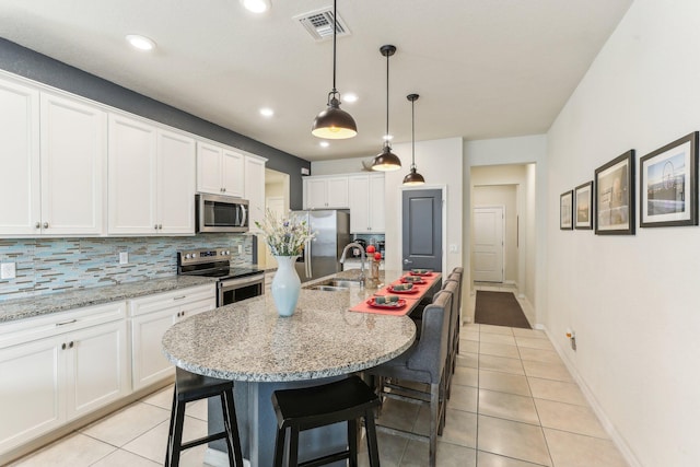 kitchen featuring a kitchen bar, a kitchen island with sink, light tile patterned floors, and appliances with stainless steel finishes