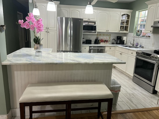 kitchen featuring decorative backsplash, light wood-type flooring, stainless steel appliances, sink, and pendant lighting