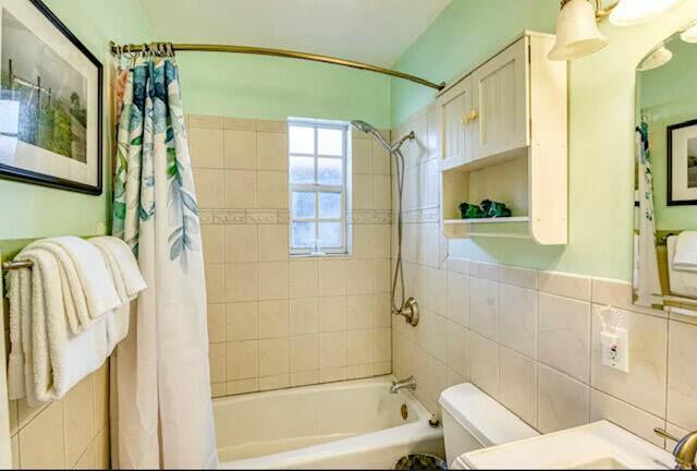 full bathroom with shower / bath combo, toilet, tile walls, and vanity