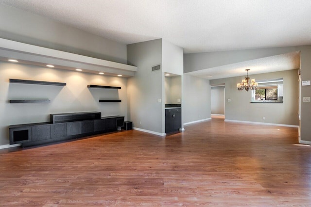 unfurnished living room featuring an inviting chandelier, lofted ceiling, hardwood / wood-style floors, and a textured ceiling