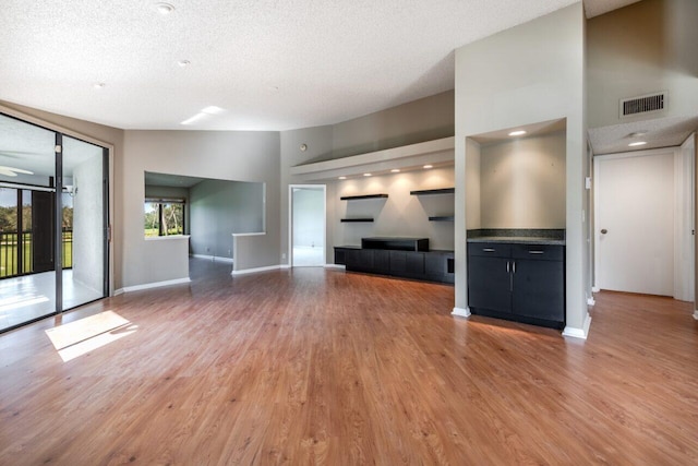 unfurnished living room with a high ceiling, hardwood / wood-style floors, and a textured ceiling