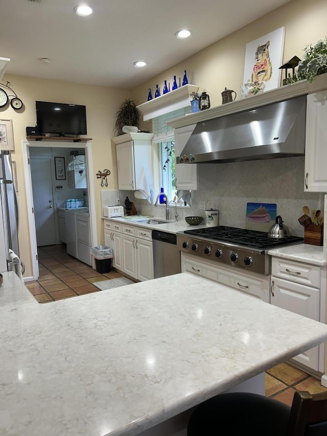 kitchen featuring decorative backsplash, stainless steel appliances, washing machine and clothes dryer, white cabinets, and range hood